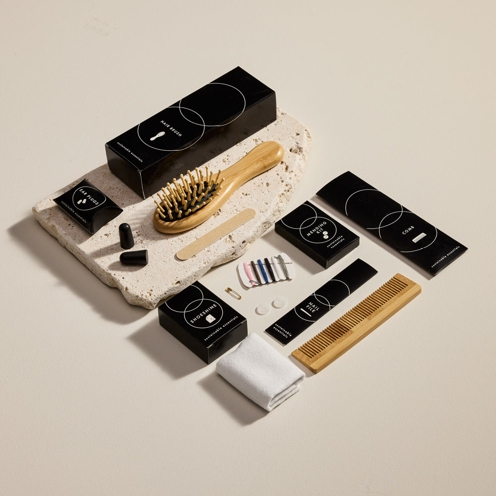 A flat lay of black boxed hotel amenity kits with matching wooden brushes arranged on stone slabs.