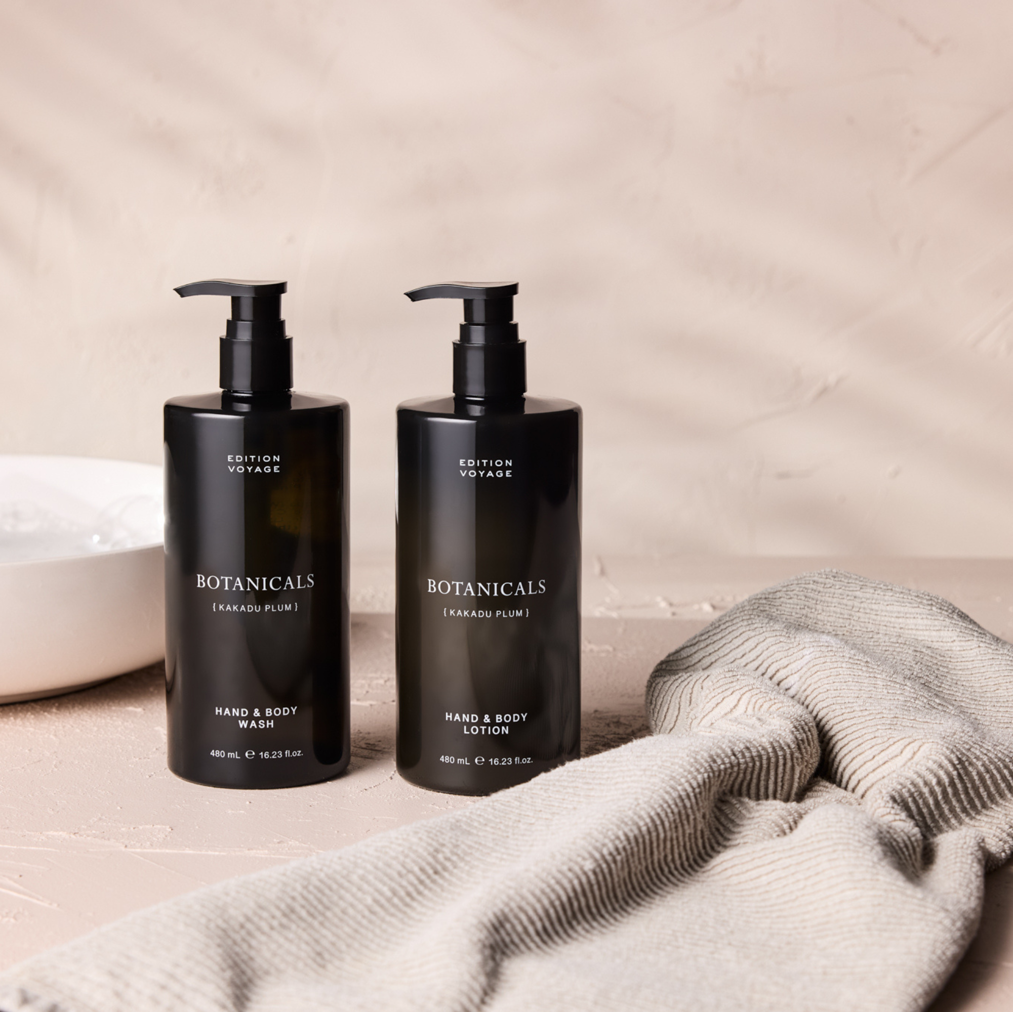 Two black Edition Voyage Botanicals pump bottles next to a folded towel on a textured surface.